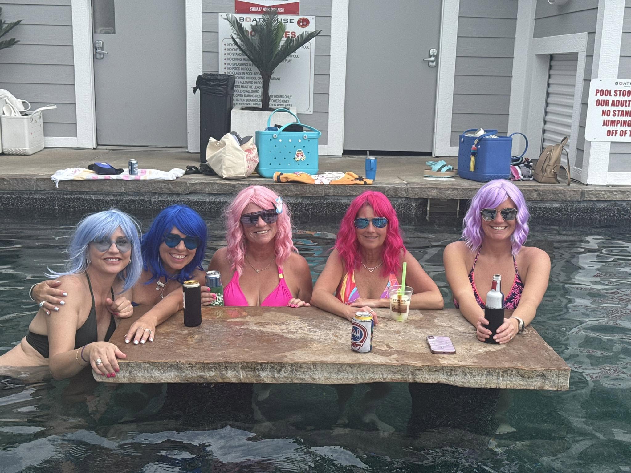 Five friends wearing colorful wigs in the Boathouse pool